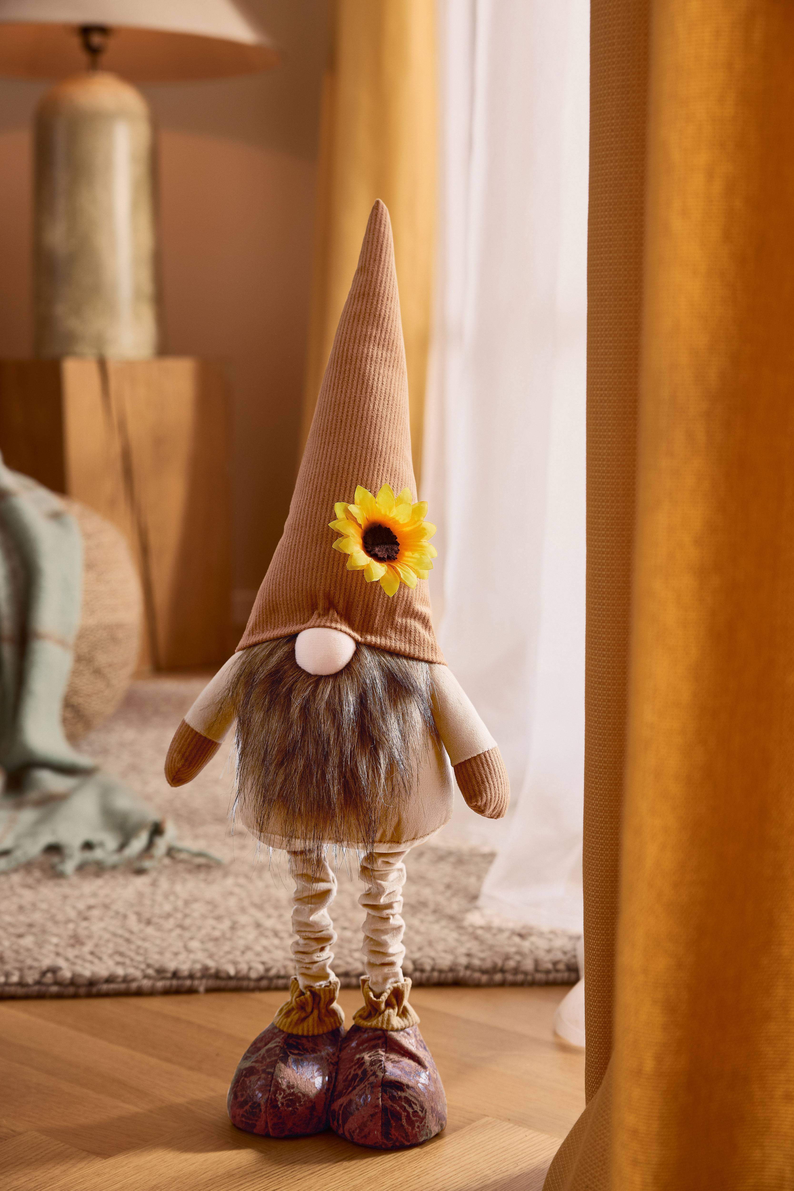 Pluche kabouter met bruine puntmuts, baard en zonnebloem, in een gezellige setting.