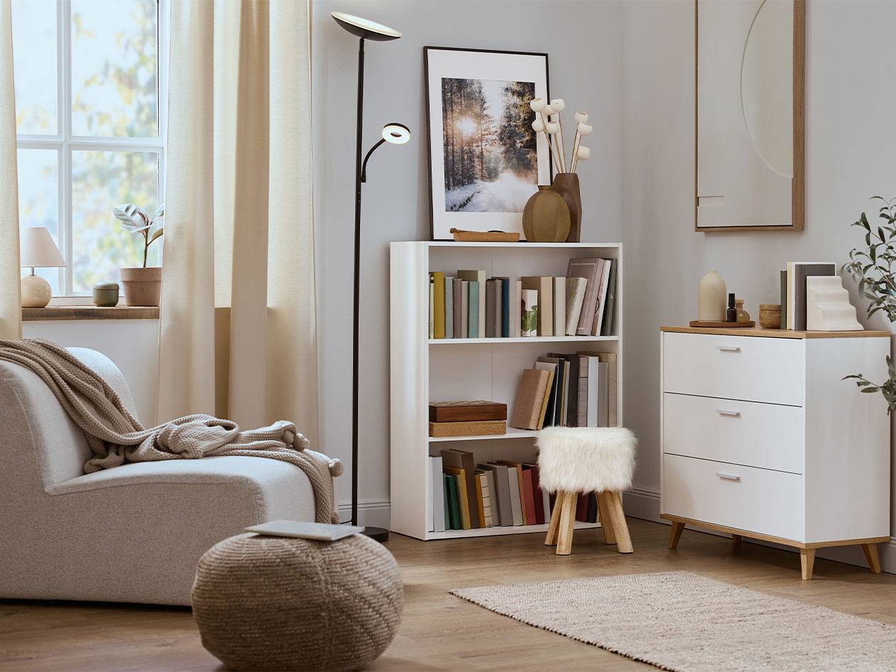 Gezellige woonkamer met fauteuil, boekenkast en ladekast in neutrale kleuren.