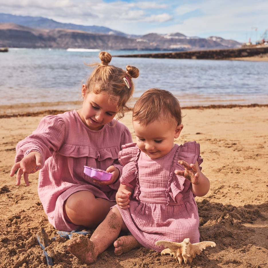 Twee meisjes in roze jurken spelen in het zand op het strand.