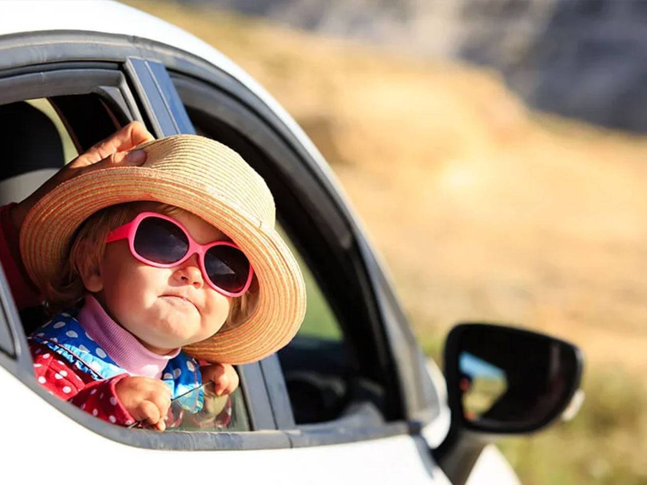 Een peuter met een hoed en zonnebril in een auto.