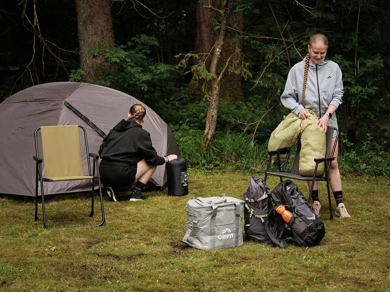 Twee personen pakken campingspullen uit, waaronder een Crivit koeltas en een tent.