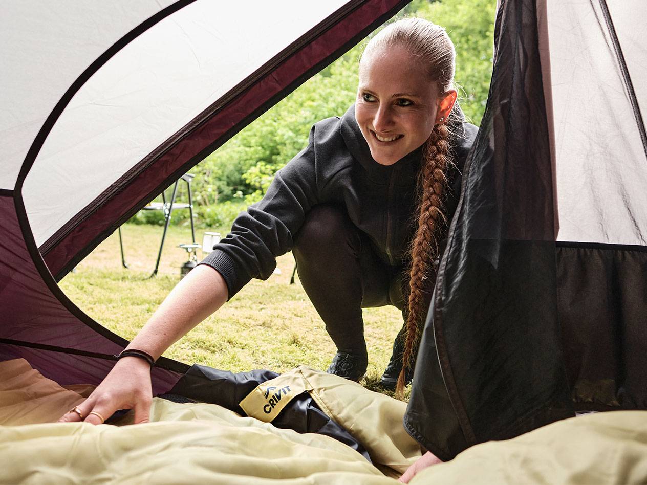Een vrouw plaatst een Crivit slaapzak in een tent.