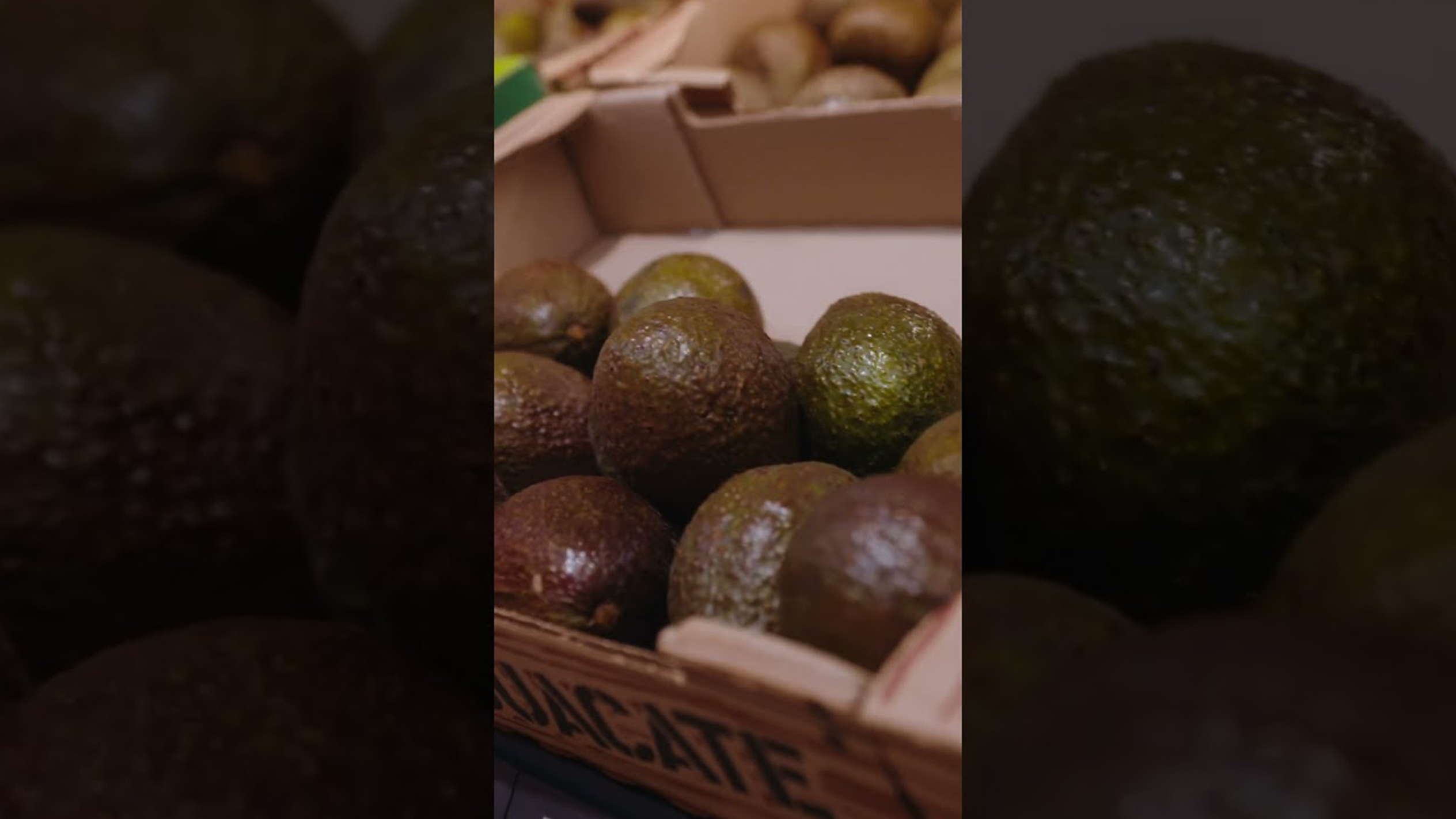 Een close-up van verse avocado's in een houten kistje met de tekst 'AVOCATE'.