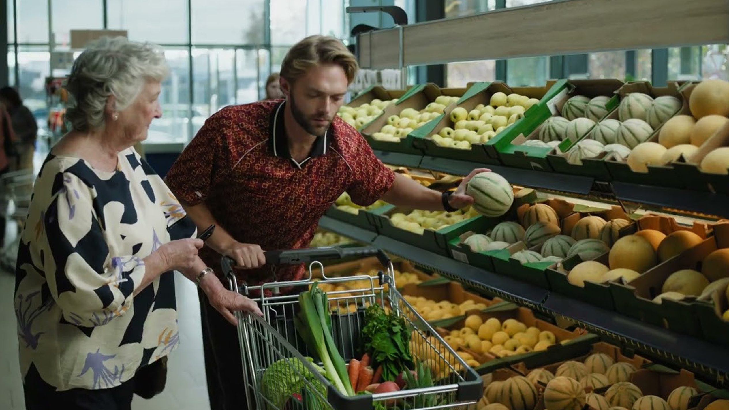 Een man en een vrouw kiezen meloenen en groenten in een supermarkt.